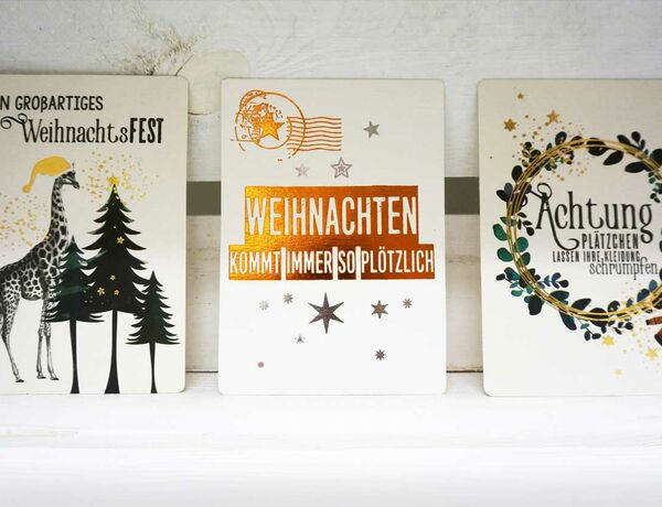 Foto dreier Weihnachtskarten aus dem Hingucker-Sortiment – mittig mit der Aufschrift „Weihnachten kommt immer so plötzlich!“